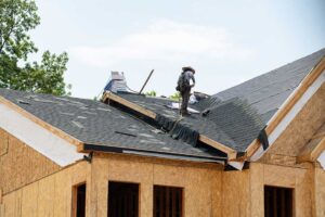 A person using binoculars to inspect a home’s shingled roof for storm damage from the yard.
