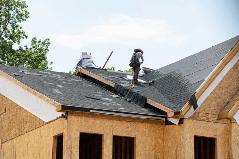 A person using binoculars to inspect a home’s shingled roof for storm damage from the yard.