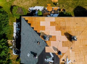 A homeowner examines aging asphalt shingles while inspecting a roof near a leafy residential home.