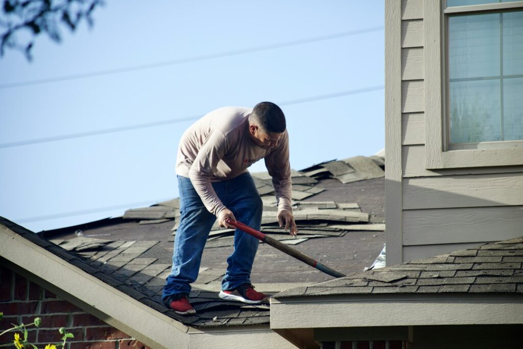 Homeowner inspecting roof gutters from the ground beside a house during autumn.