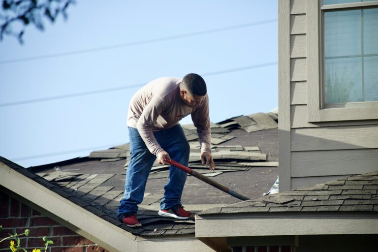 Homeowner inspecting roof gutters from the ground beside a house during autumn.